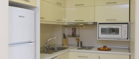 A compact kitchen with white cabinets, a built-in microwave, a dishwasher, and a sink.