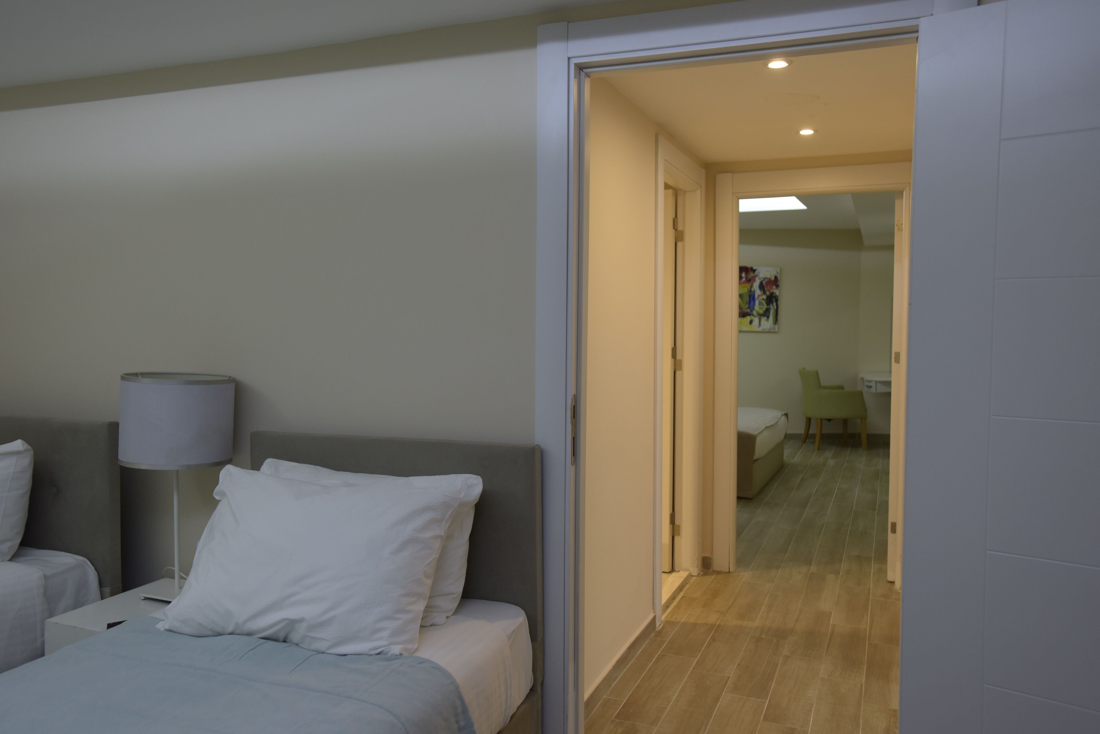A hotel room with a bed, a bedside table with a lamp, and a view into the adjacent room.