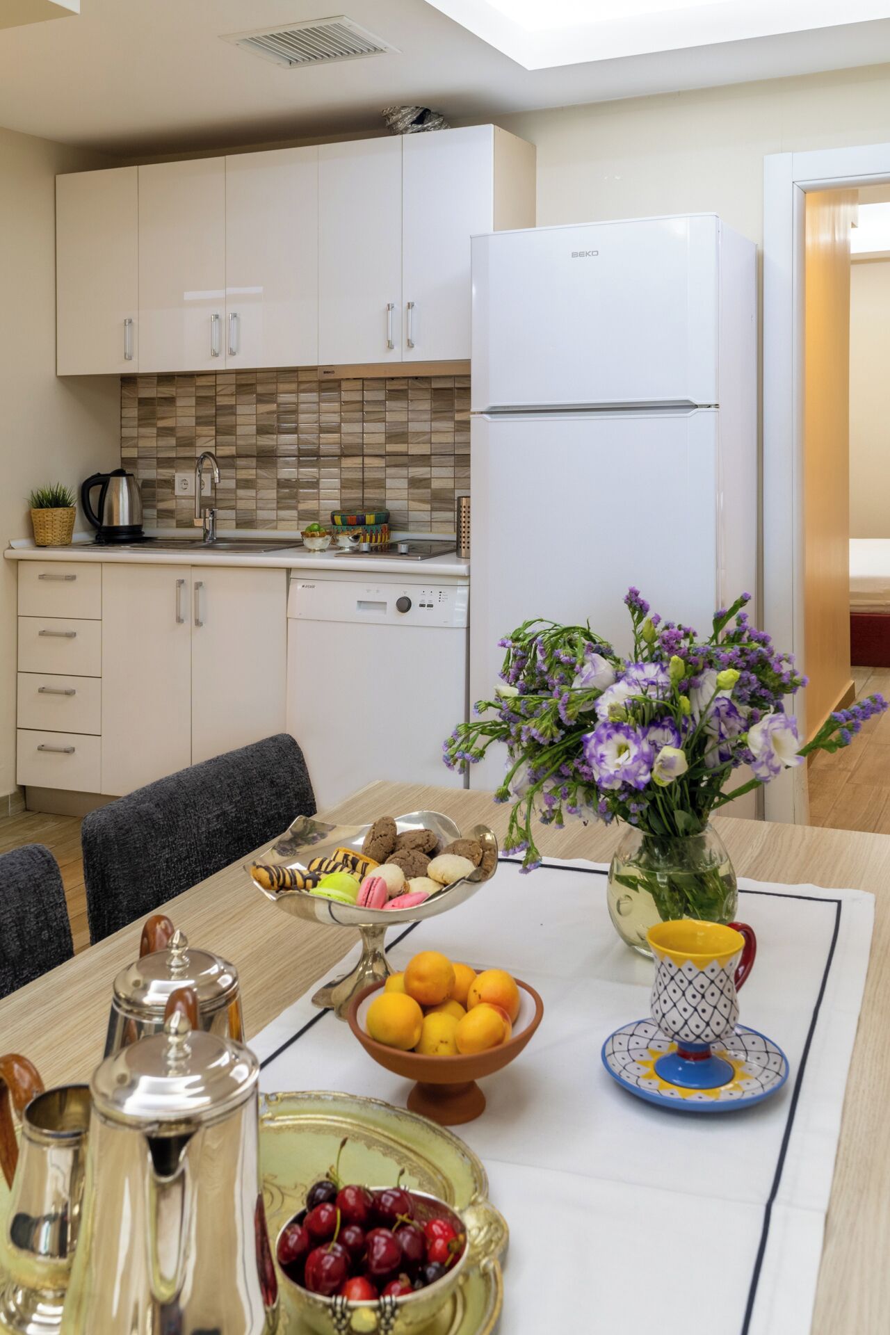 Una cocina moderna con armarios blancos, un refrigerador blanco y una zona de comedor con una mesa dispuesta para dos.