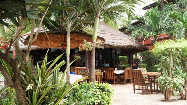A rustic outdoor seating area with thatched-roof structures, surrounded by lush greenery and tropical plants. - Napoleon Lagune (Lomé)
