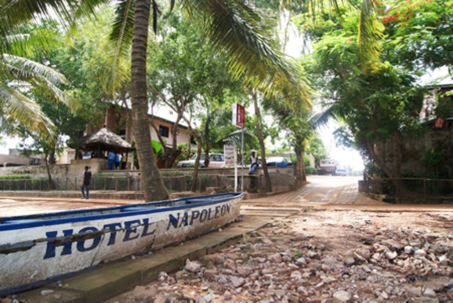A boat with 'HOTEL NAPOLEON' written on it, parked by a road with palm trees and a building in the background.