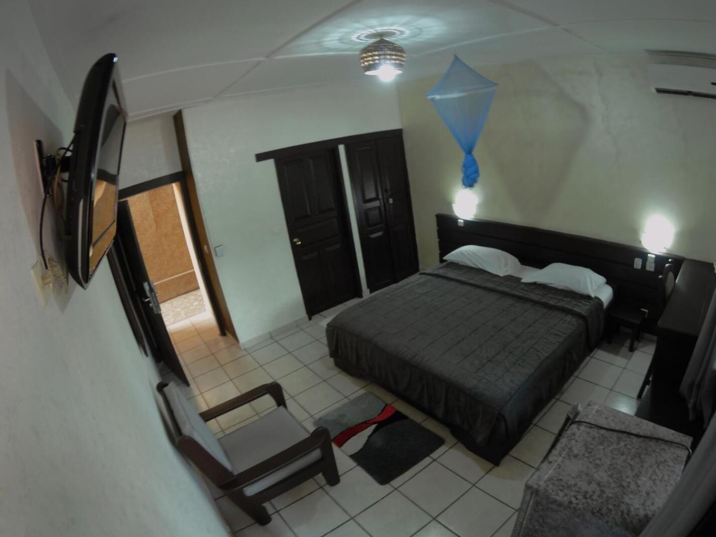 Un dormitorio con cama, mesitas de noche, escritorio, silla, televisor y ventilador de techo.