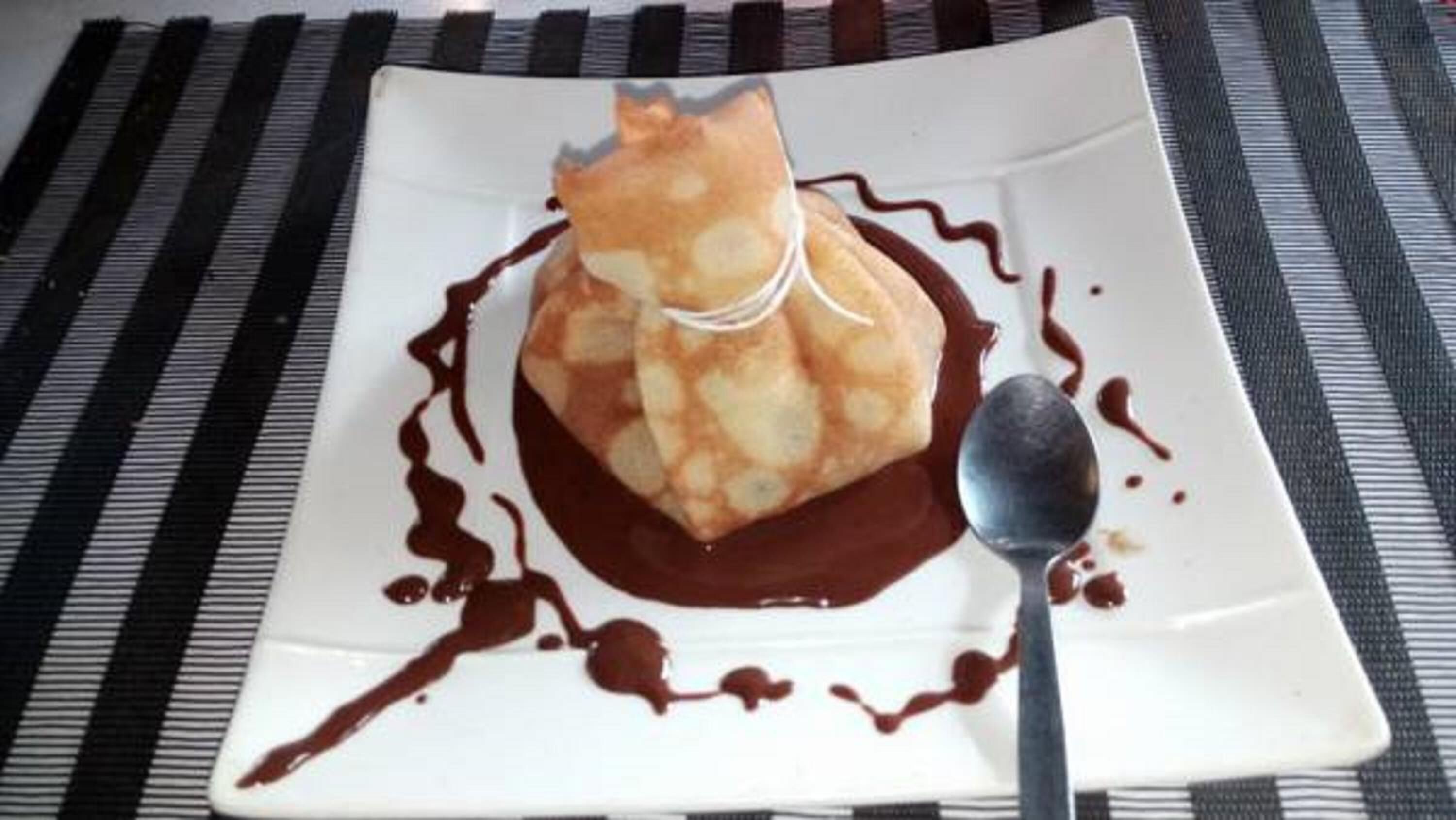 Un postre en un plato blanco con salsa de chocolate y una cuchara.