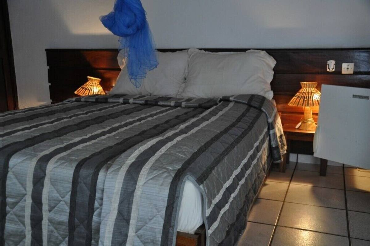Uma cama com colcha listrada, duas luminárias de cabeceira e uma cadeira branca.