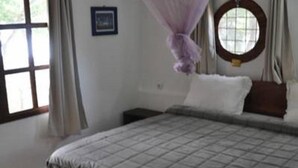 A bedroom with a bed, a window with curtains, a bedside table, and a hanging mosquito net. - Napoleon Lagune (Lomé)