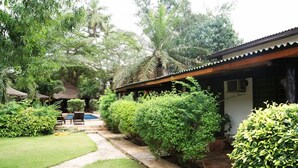 A well-maintained garden with a swimming pool, a covered seating area, and a building with a tiled roof. - Napoleon Lagune (Lomé)