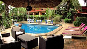 A pool area with lounge chairs and tables, surrounded by greenery and a building in the background. - Napoleon Lagune (Lomé)
