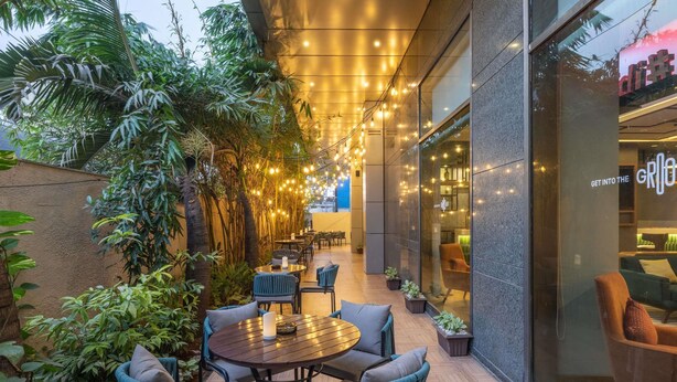 An outdoor seating area with round tables and chairs, surrounded by lush greenery and string lights. - ibis Mumbai Airport Hotel (Mumbai)