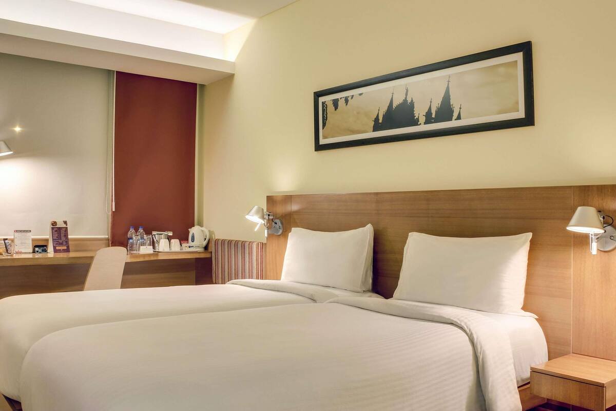 A hotel room with a large bed, a desk with a chair, a coffee station, and a framed picture on the wall.