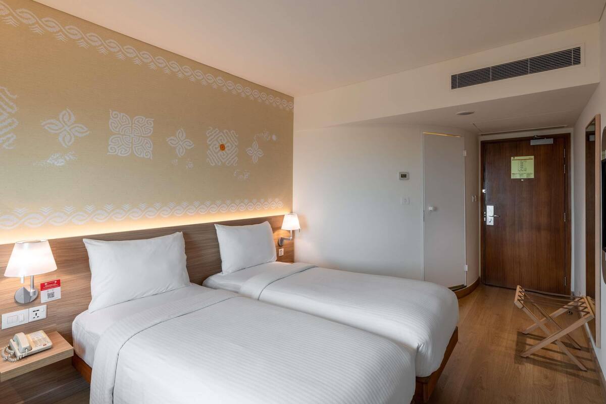 A hotel room with two beds, a bedside telephone, and a lamp.