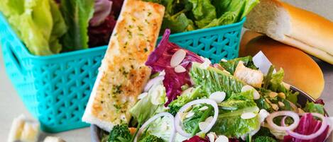 A bowl of salad with various vegetables and croutons, a piece of grilled bread, and a baguette on a table.