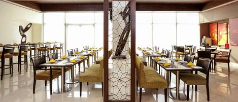 A spacious dining area with multiple tables and chairs, a decorative column, and large windows providing natural light.