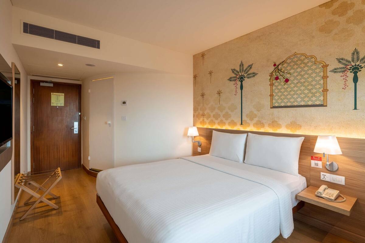 A hotel room with a large bed, two bedside tables with lamps, a wall-mounted phone, and a door with a sign.