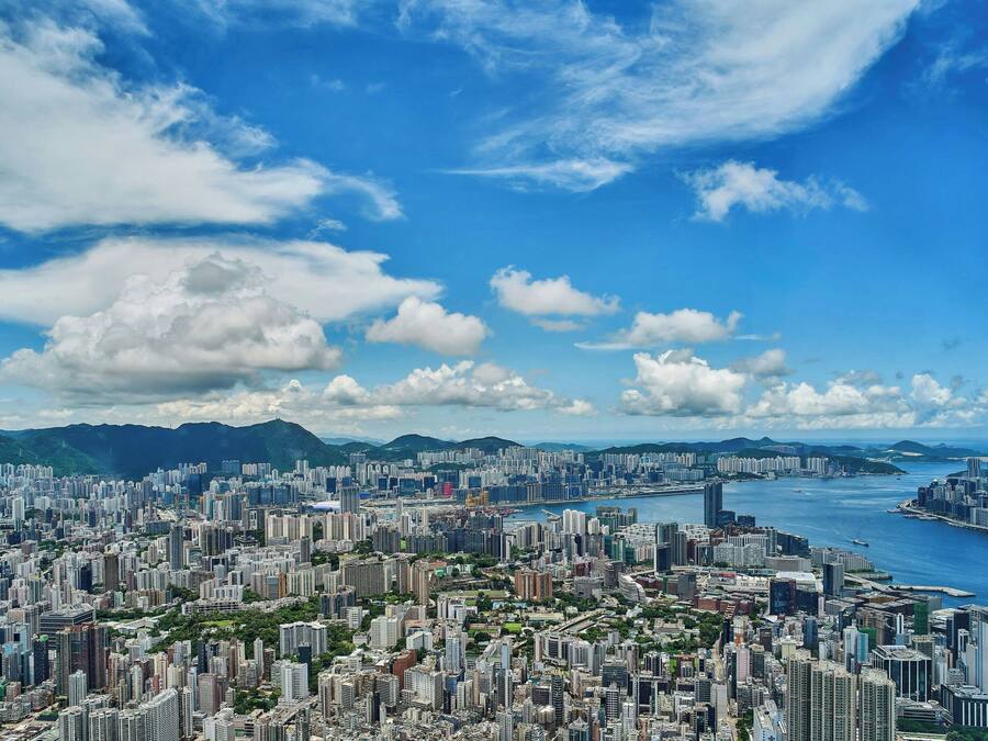 Une vue urbaine avec de hauts immeubles, une étendue d’eau et des montagnes en arrière-plan.