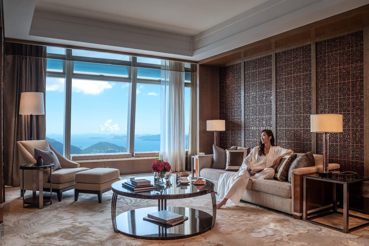 A spacious living room with a large window offering a view of the mountains, a round coffee table with books and a vase, and a patterned wall.