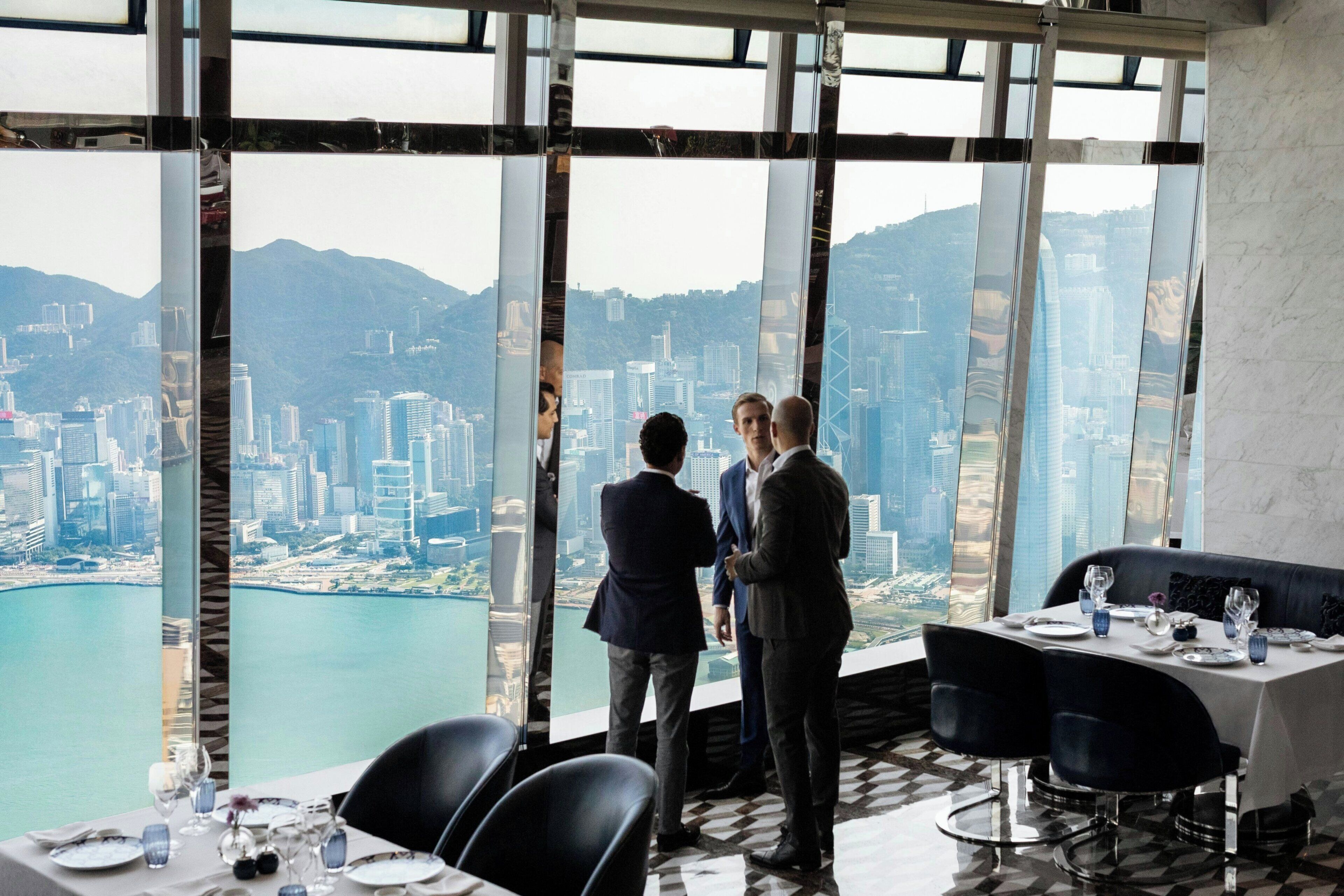 A high-rise dining area with a panoramic city view, modern furniture, and a table set for a meal.