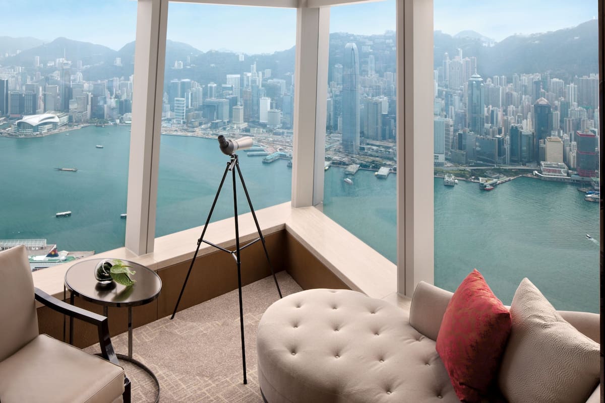 A high-rise room with a panoramic city view, a telescope, and a seating area with a view of the harbor.
