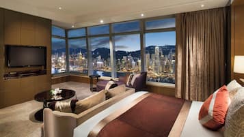 A hotel room with a large bed, a sofa, a TV, and a view of a cityscape at night.