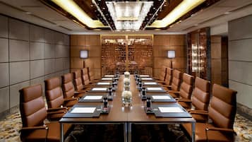 A conference room with a long table, brown leather chairs, and a chandelier.