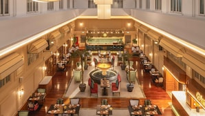 A spacious hotel lobby with multiple dining areas, a central fountain, and a bar.