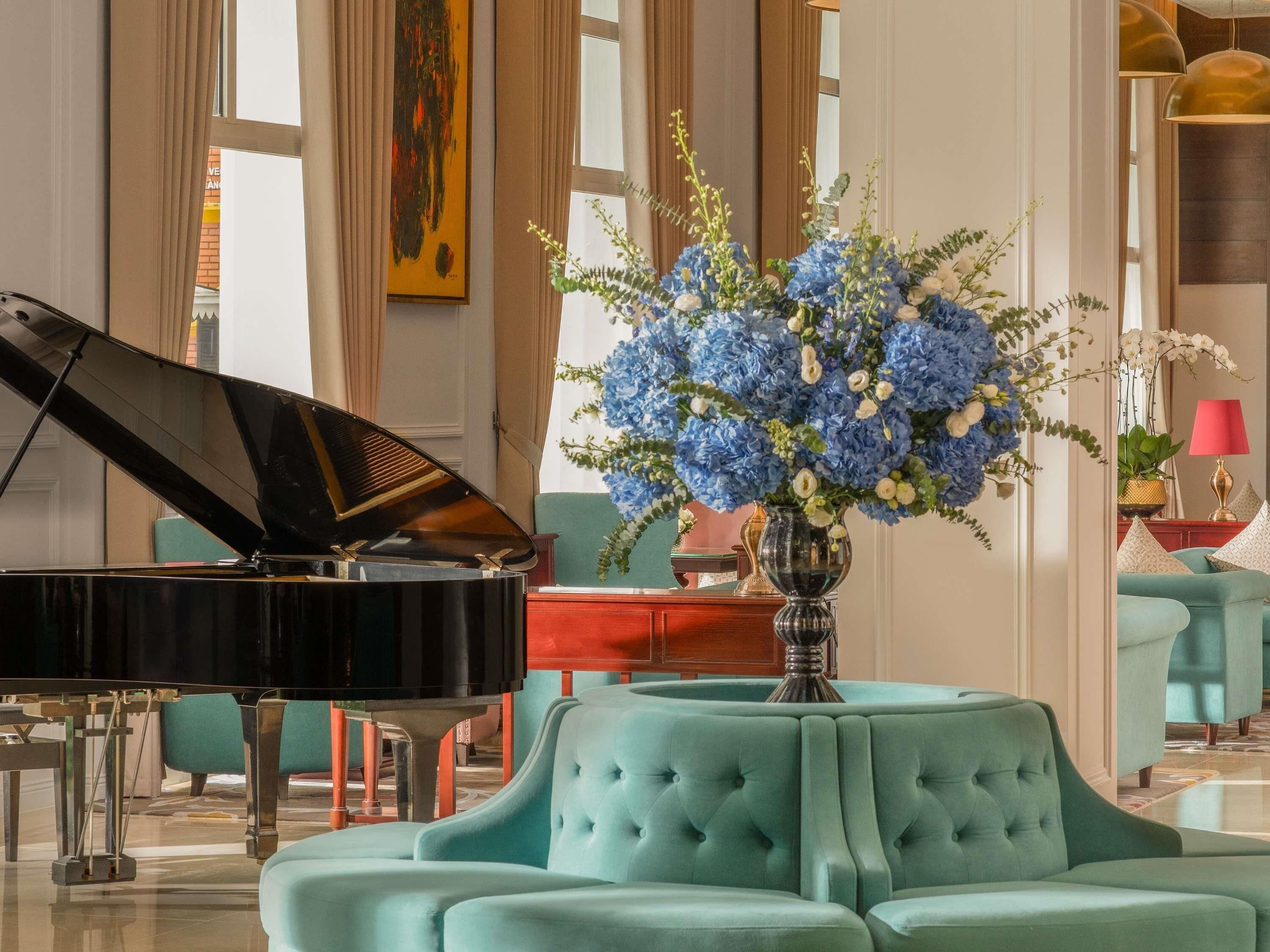 A grand piano in a spacious room with a large floral arrangement and teal upholstered seating.
