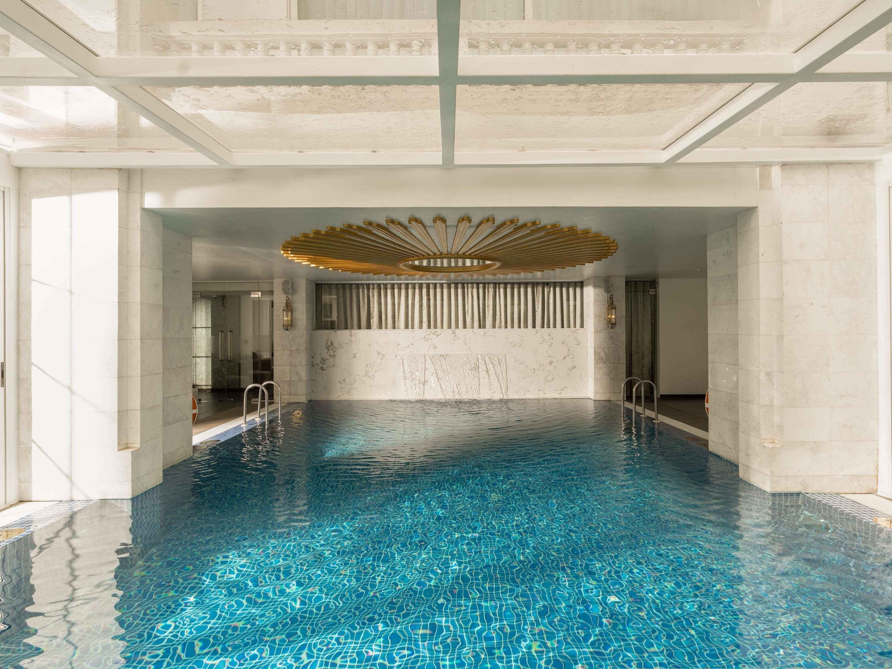 Una amplia piscina interior con agua cristalina, un diseño de techo moderno y paredes de mármol.