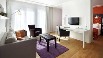 A modern hotel room with a sofa, a desk, a TV, and a bed.