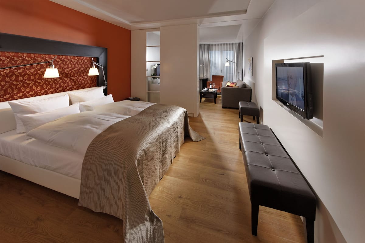 Quarto de hotel moderno com uma cama grande, um banco, uma televisão e uma mesa de trabalho com uma cadeira.