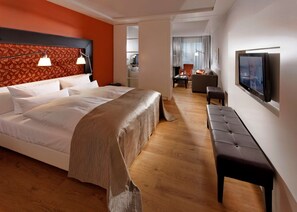 A modern hotel room with a large bed, a bench, a TV, and a view into the dining area. - Parkhotel Stuttgart Messe - Airport (Leinfelden-Echterdingen)