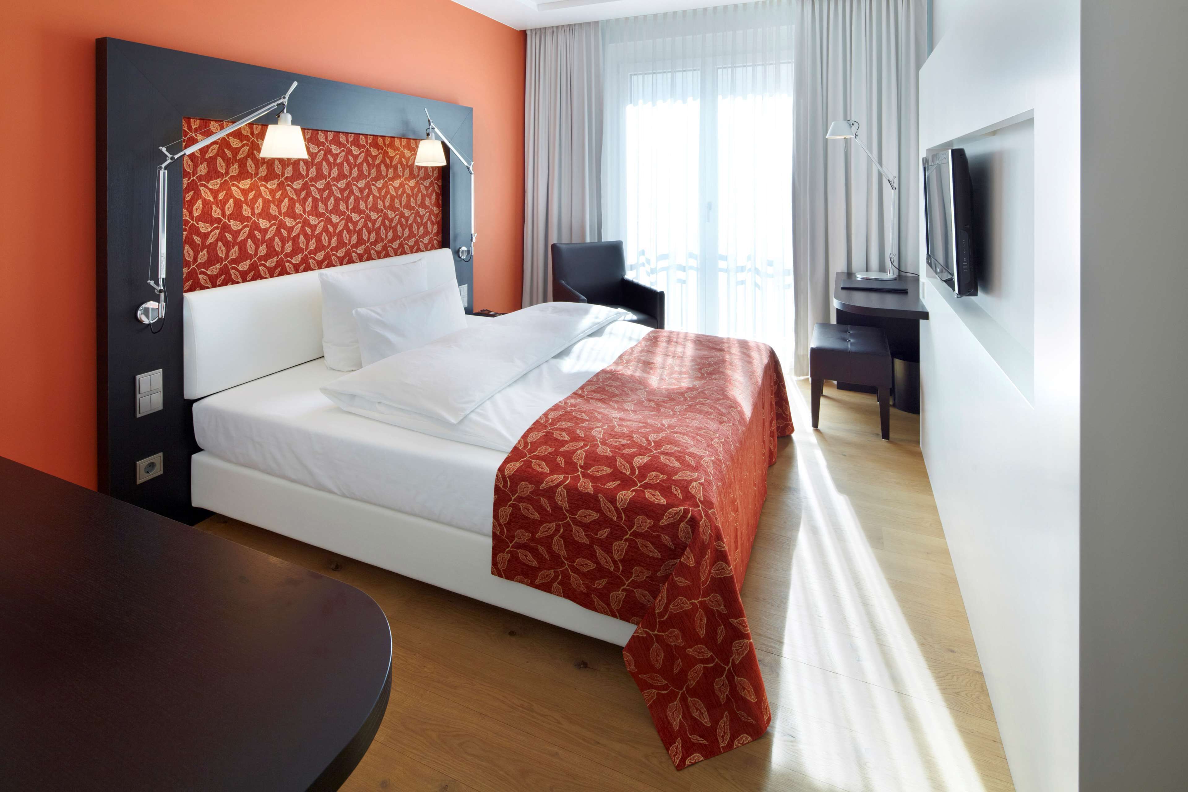 A hotel room with a bed, a desk, a TV, and a window with curtains.