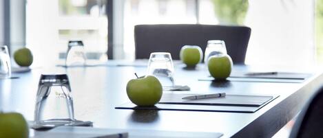 A conference table with green apples, glasses, and a pen.