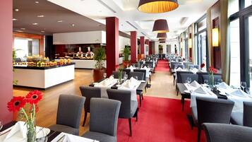Une salle à manger d’hôtel avec des tables dressées pour le service, un buffet central et de grandes fenêtres le long des murs.