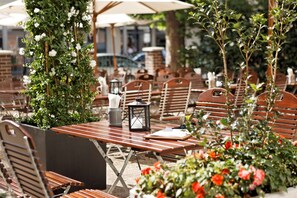 An outdoor cafe with wooden tables and chairs, a planter with white flowers, and a lantern.