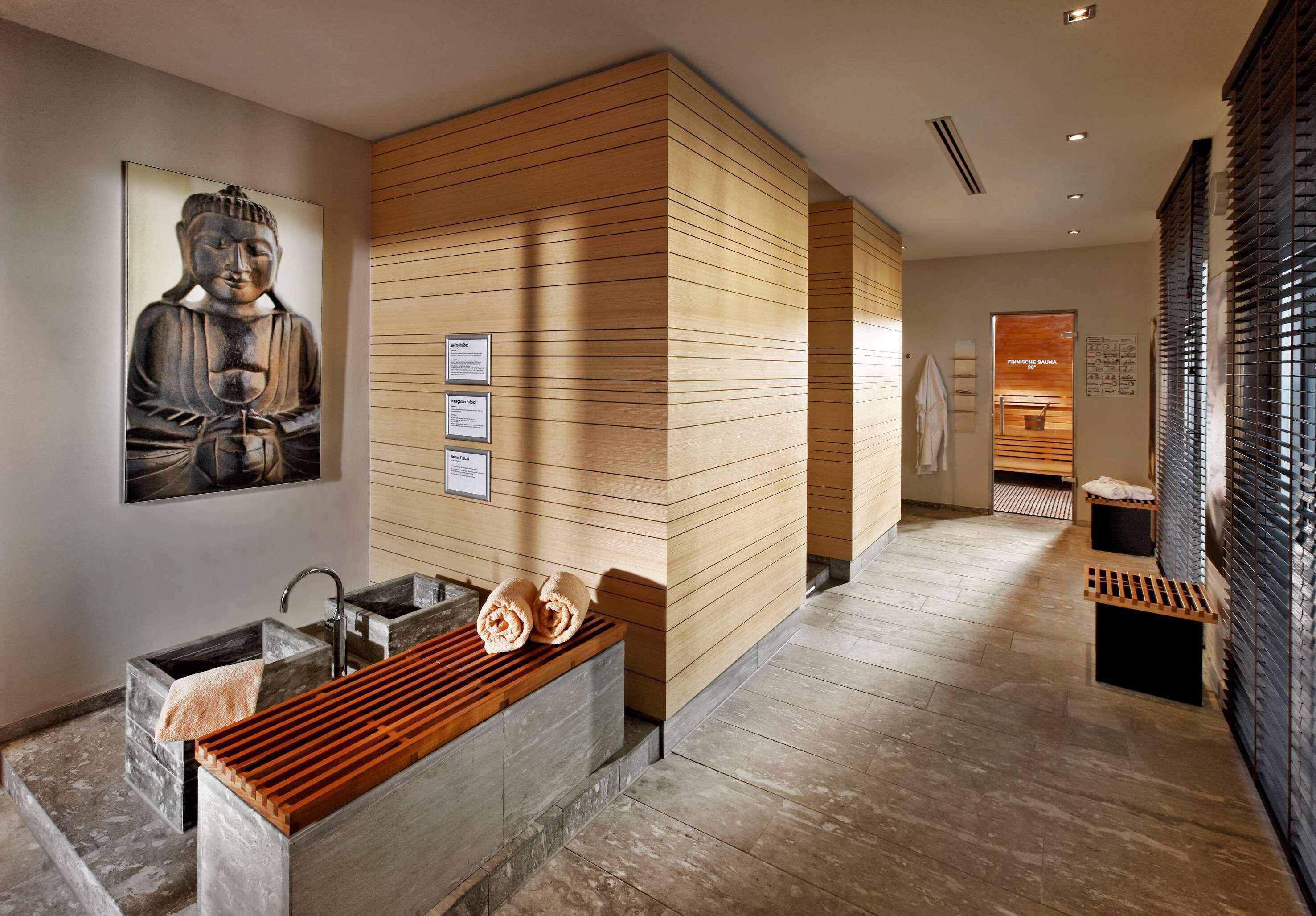 A modern spa area with a wooden wall, a Buddha statue, a sink, and a bench with towels.