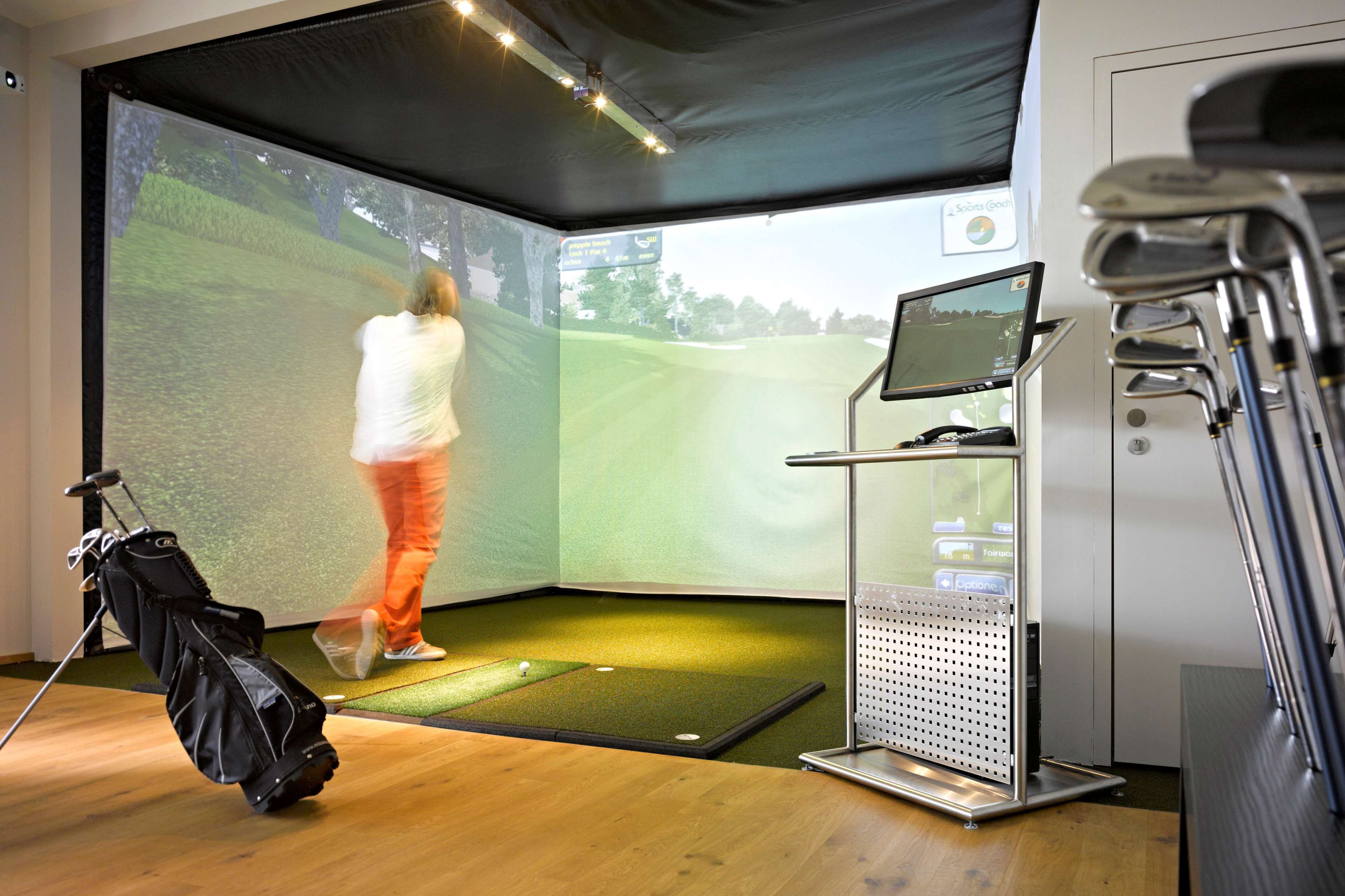 A golf simulation room with a screen displaying a golf course, a golf bag, and a golf cart.