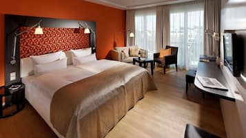 A hotel room with a large bed, a desk with a chair, a TV, and a view of the city.