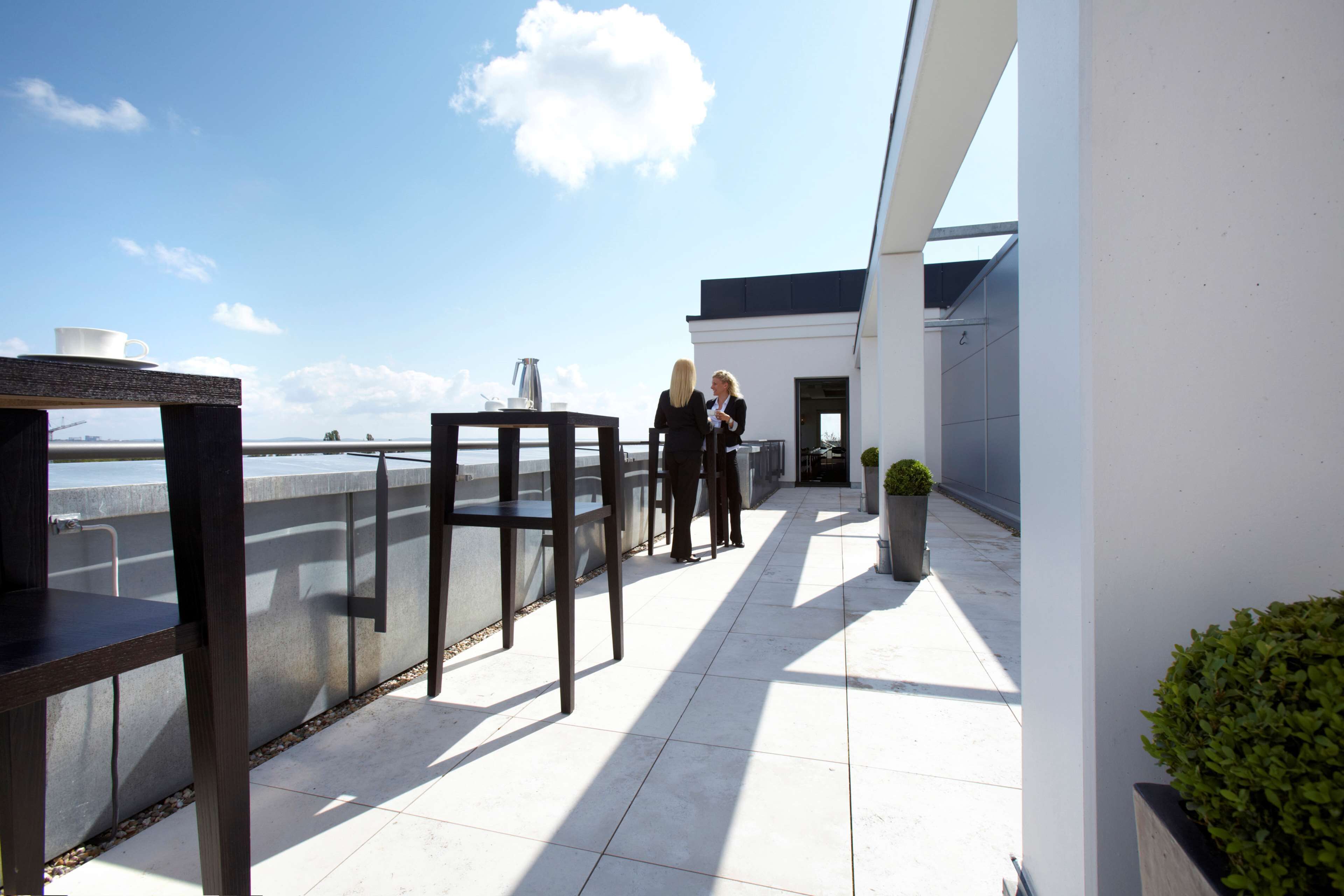 A rooftop terrace with a clear view of the sea, a table with a cup and a pitcher, and a potted plant.