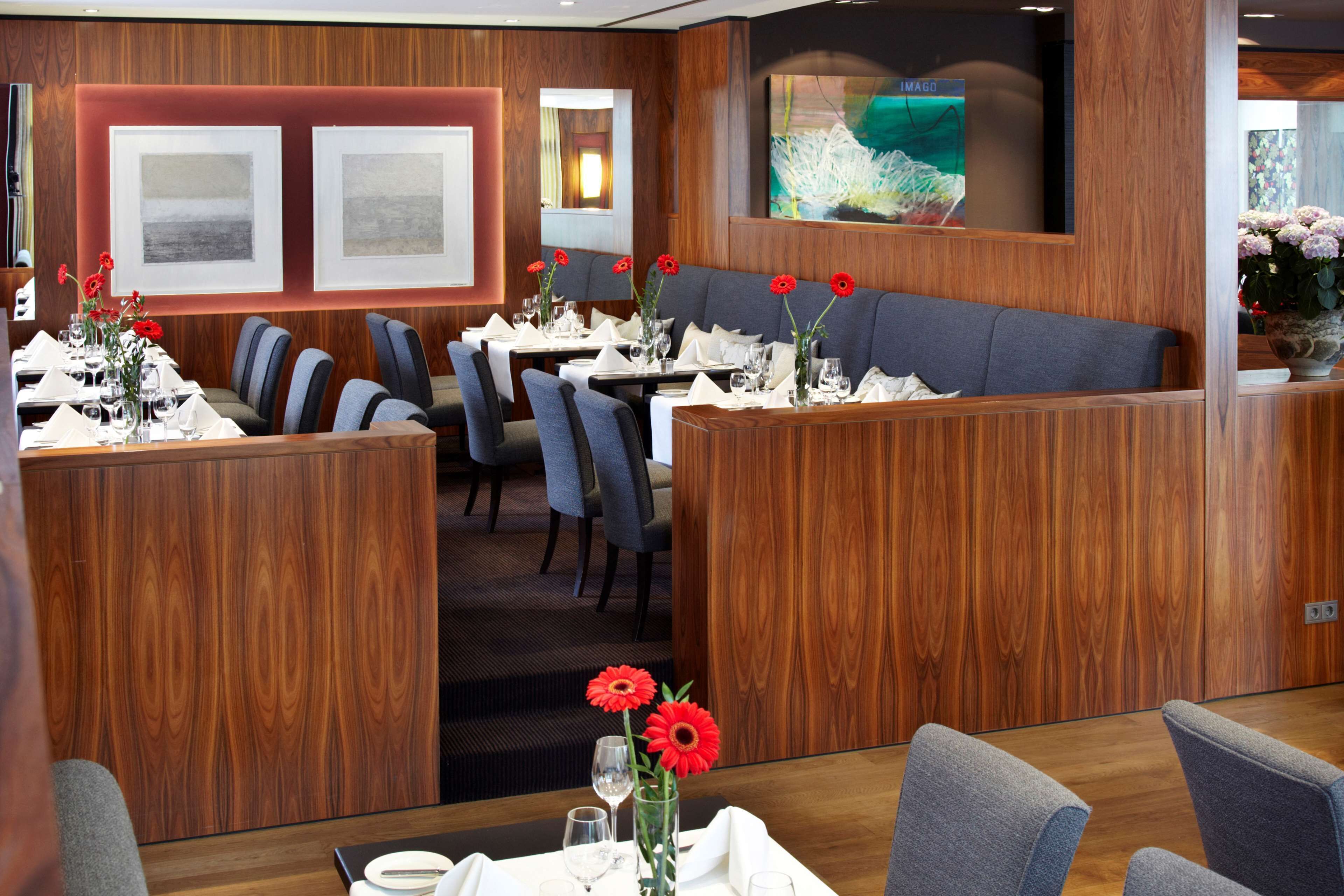 A restaurant with wooden paneling, tables set with white tablecloths, and red flowers in vases.