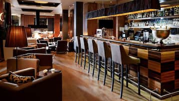 Zona de bar con taburetes de madera, barra con botellas y área de estar con sofás y lámparas.