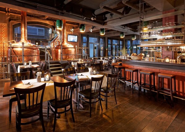A restaurant interior with wooden tables and chairs, a bar area, and large windows.