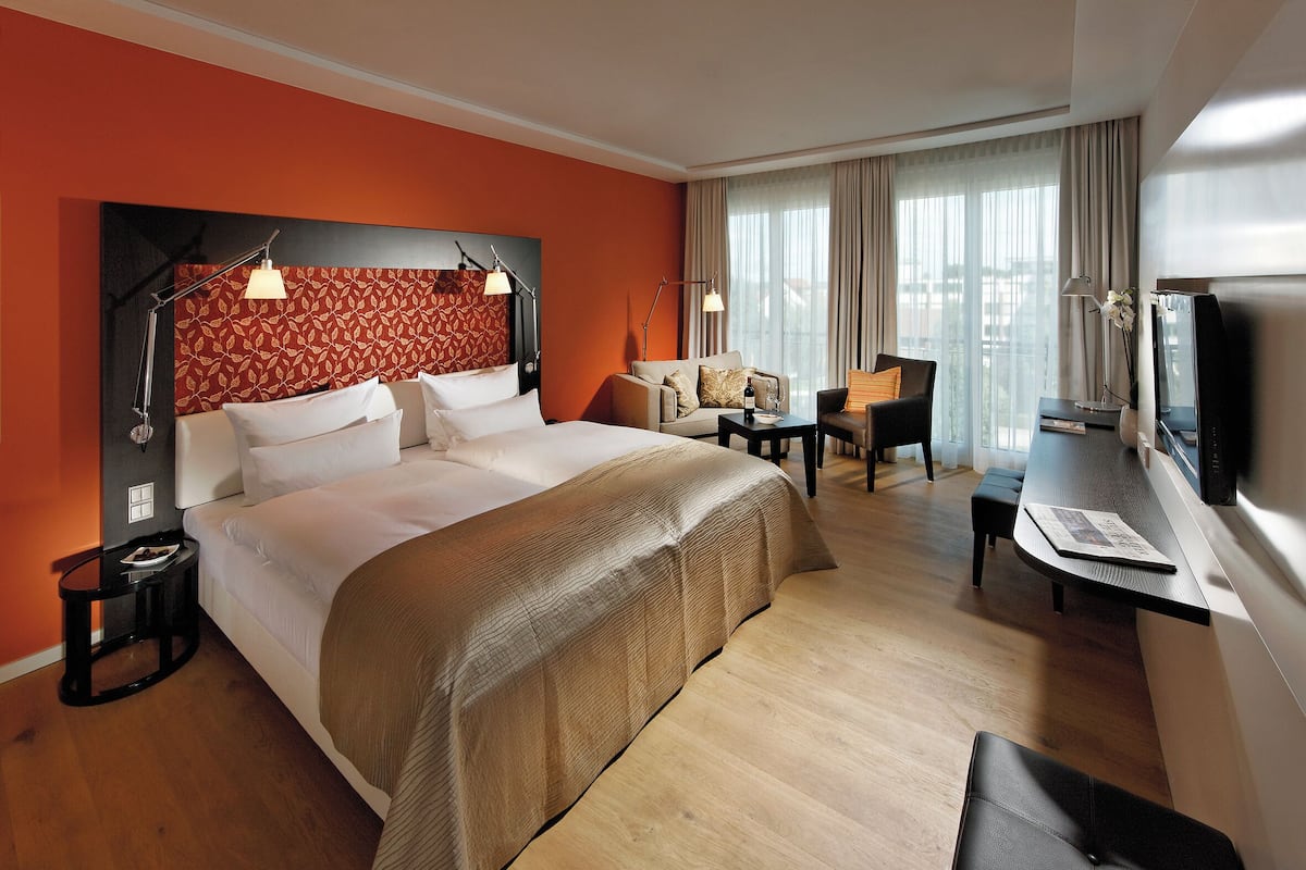 Quarto de hotel com uma cama grande, escrivaninha, cadeira e televisão.