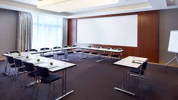 Un salón de conferencias con una pantalla grande, varias mesas y sillas.
