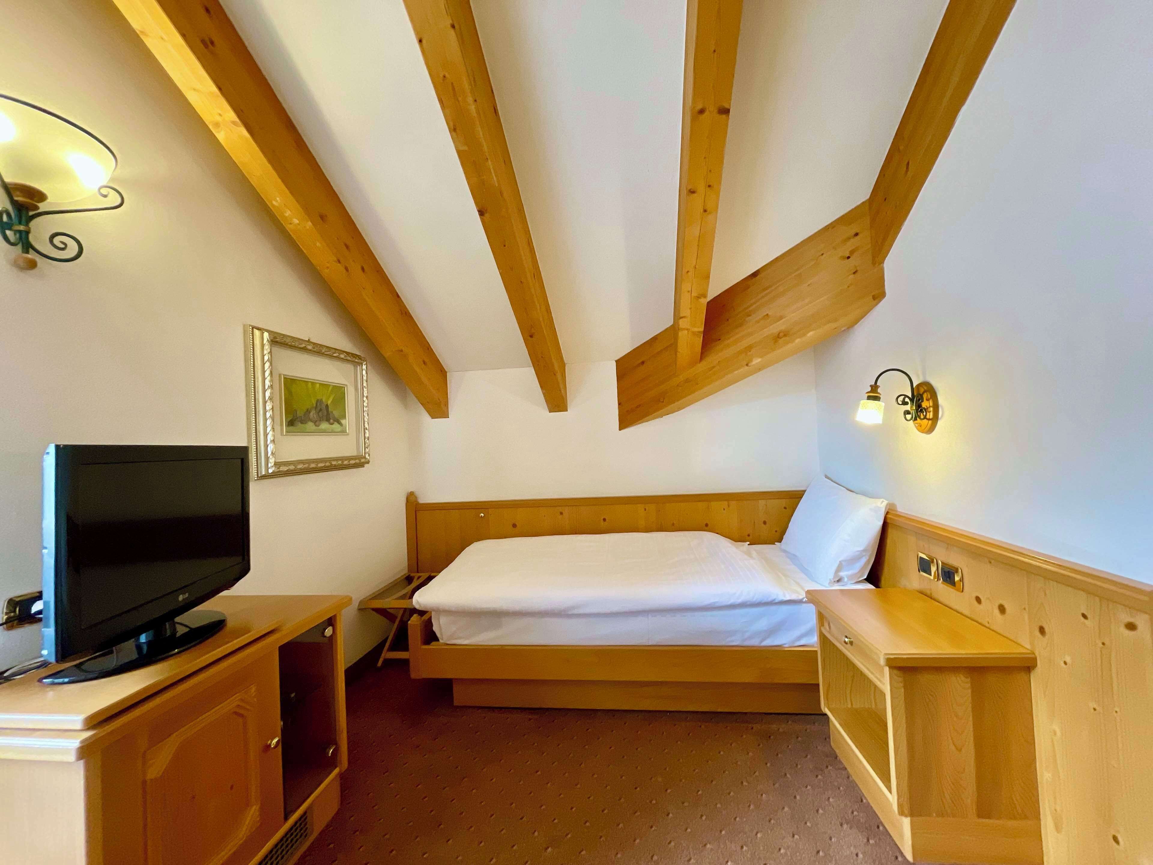 Ein Schlafzimmer mit Bett, Holzbalken, einem Fernseher auf einem Schrank und Wandleuchten.