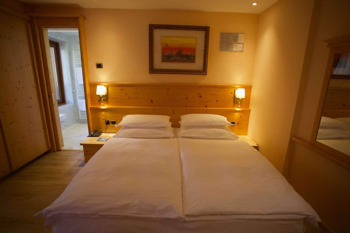 Una cama doble con dos mesitas de noche, cada una con una lámpara, en una habitación con paneles de madera y un cuadro en la pared.