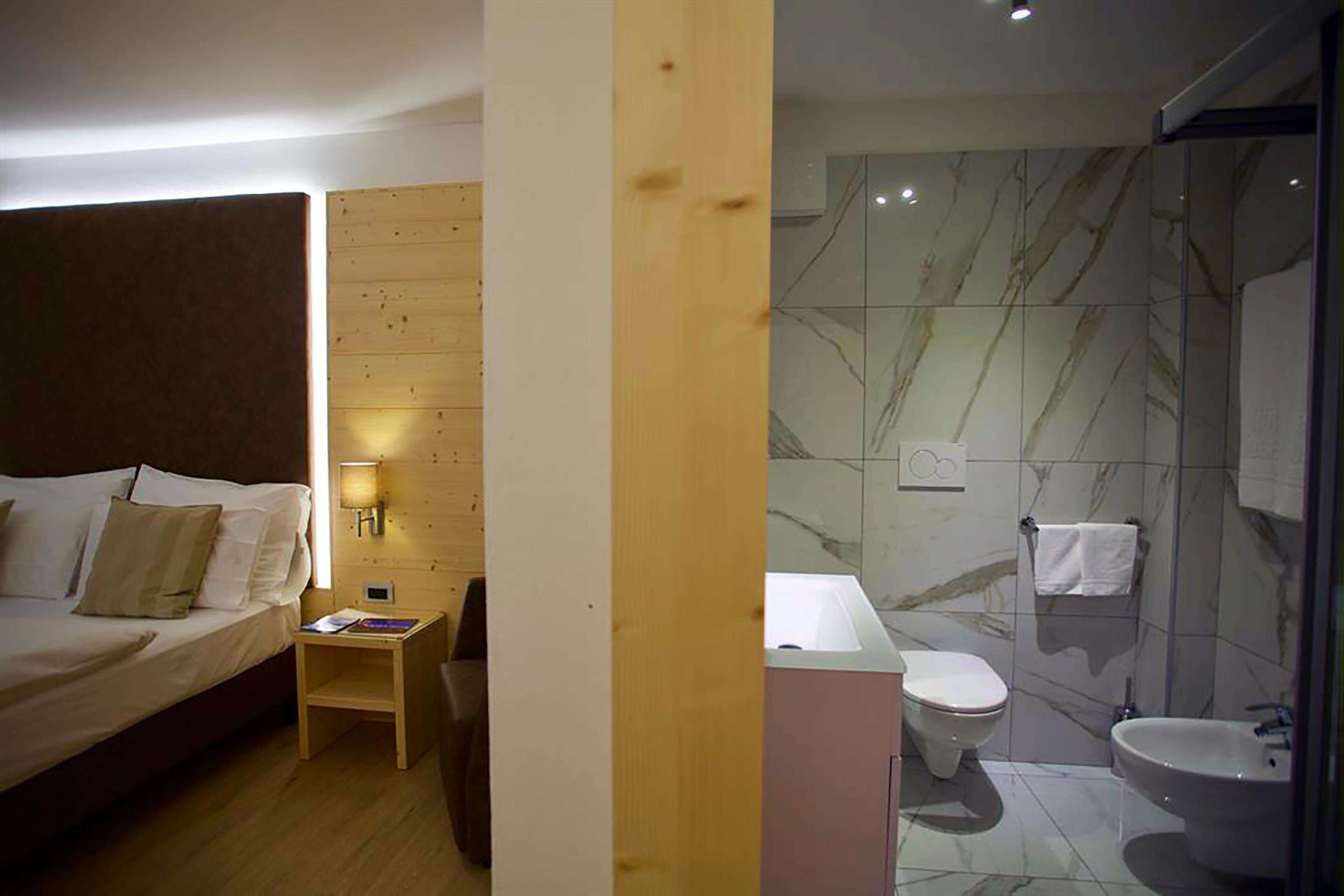 Une chambre d’hôtel comprenant un lit, une table de chevet, une lampe et une salle de bain avec des toilettes, un lavabo et des murs en marbre.
