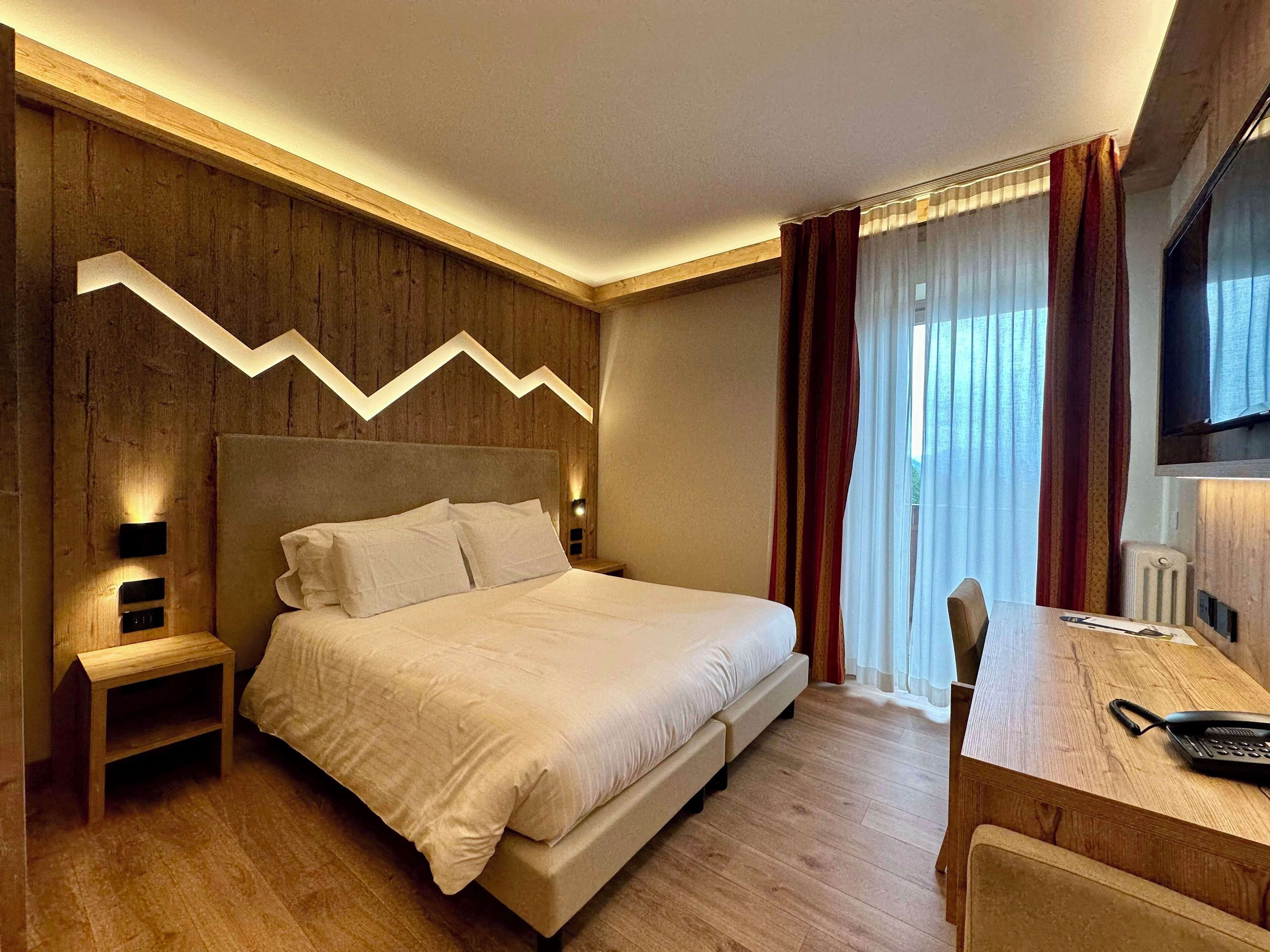 Une chambre d’hôtel moderne dotée d’un grand lit, de lambris en bois, d’un bureau avec un téléphone et d’un téléviseur fixé au mur.