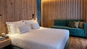 A bedroom with a large bed, a green sofa, wooden panel walls, and a nightstand with books.