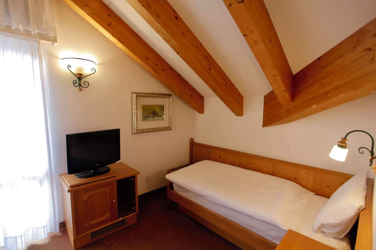 Un dormitorio con techo de madera, una cama, un televisor sobre un mueble de madera y dos luces fijadas a la pared.