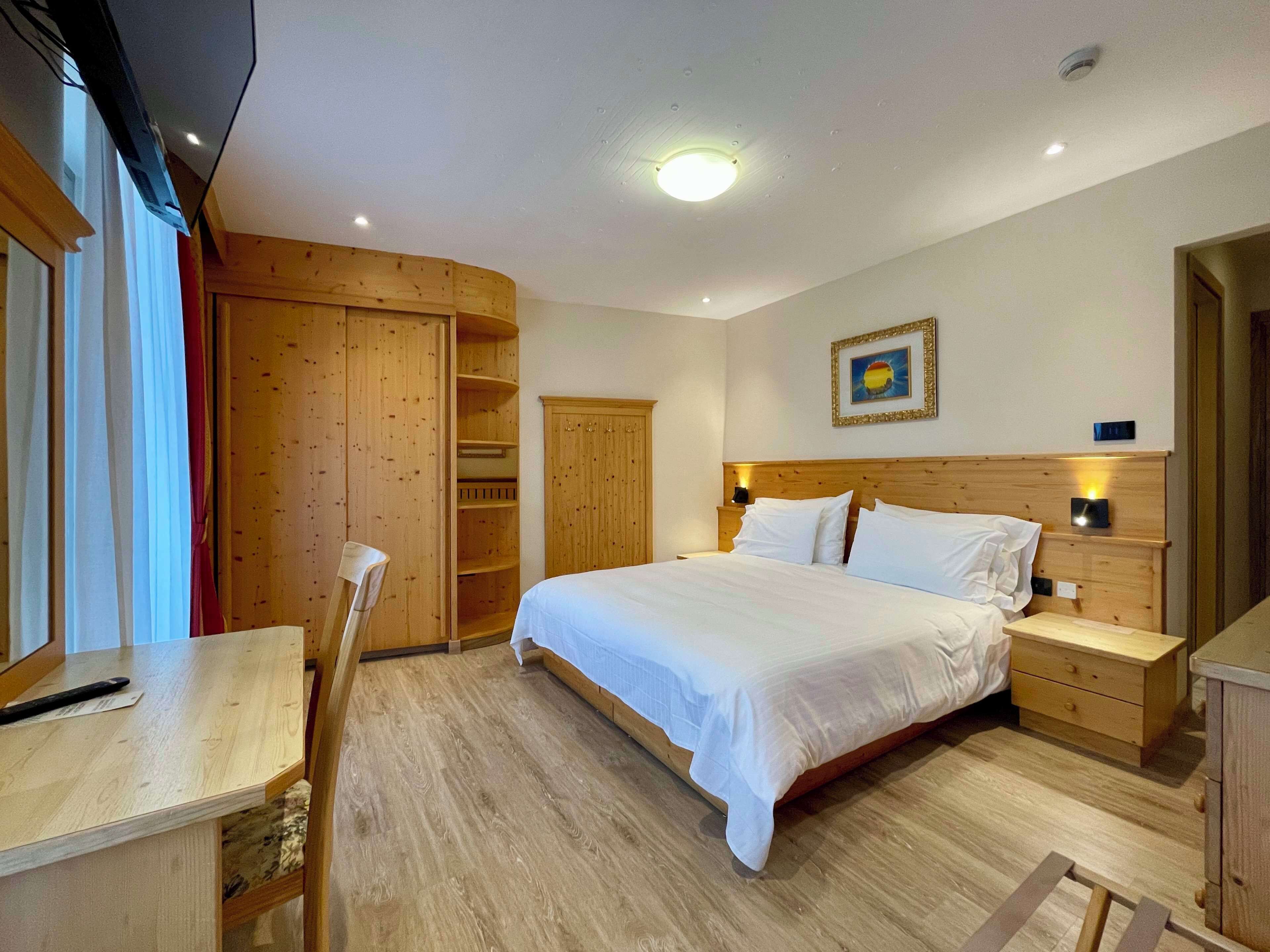 Une chambre à coucher comprenant un lit, une armoire en bois, une table de chevet et un bureau avec une chaise.