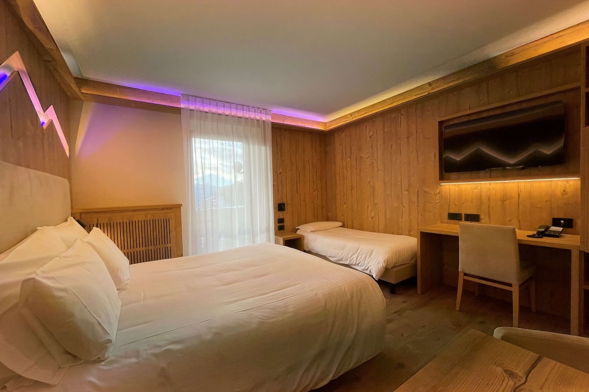 Una habitación de hotel con una cama grande, una cama más pequeña, un escritorio y una silla.